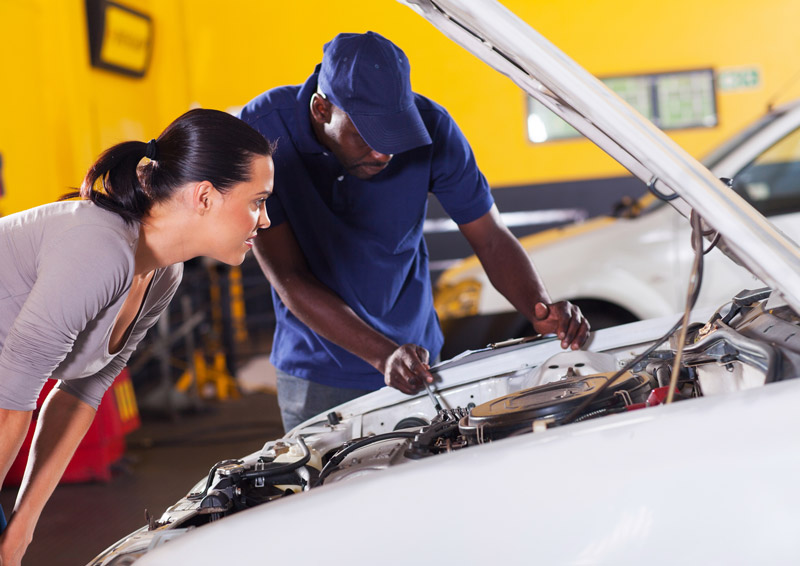 A mechanic looks under the hood of a car with a female customer in an auto service garage