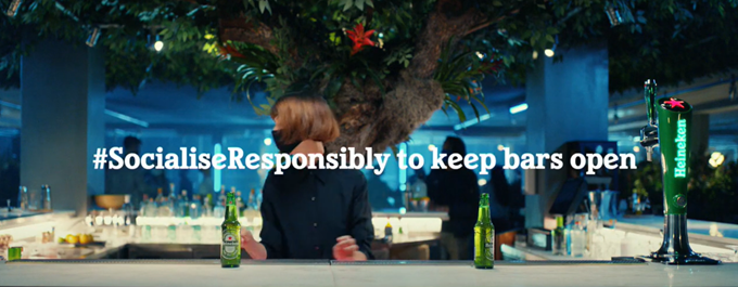 Heineken beer ad showing a woman social distancing and wearing a mask in a bar