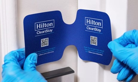Rubber gloves put a Hilton CleanStay seal on a door to assure guests that hotel rooms are COVID safe